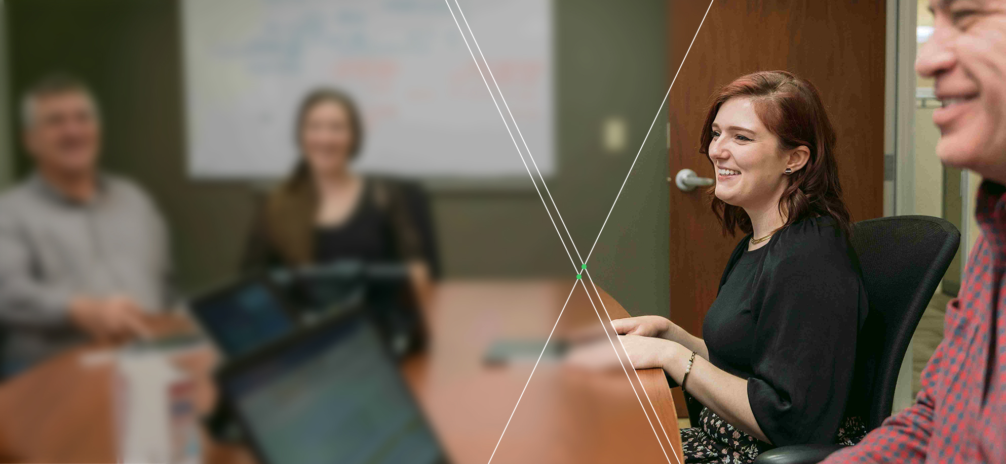 Four people sit around a conference table; two are in focus, while two are blurred in the background.