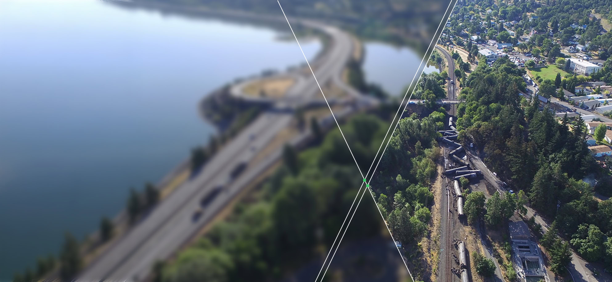 Aerial view of a highway by a body of water on the left and a residential area with trees and train tracks on the right, divided by lines.